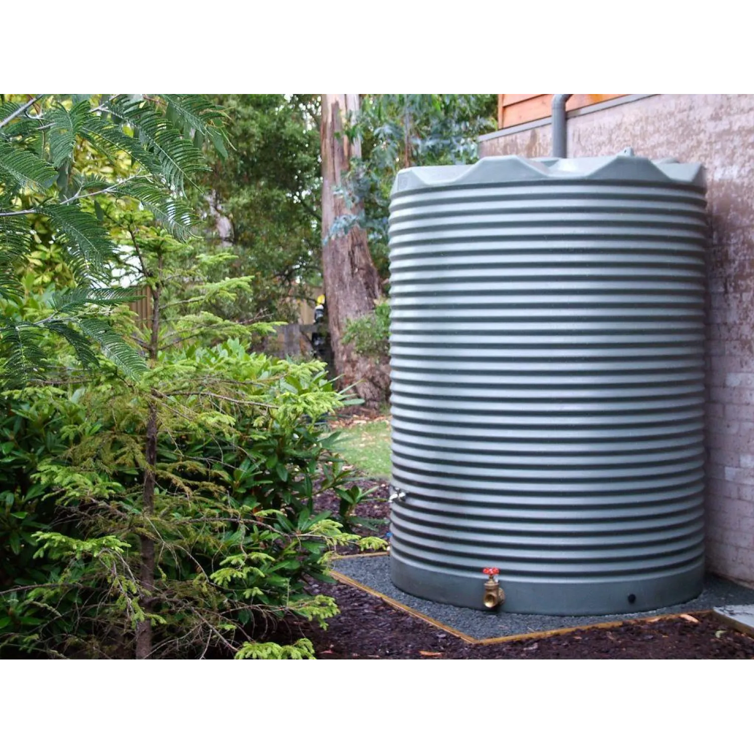 4600 Ltr Corrugated Rainwater Tank on gravel base with ferns and brick wall