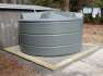6300 Ltr Panelled Wall Rainwater Tank in Slate Grey next to garden shed with gravel and timber base