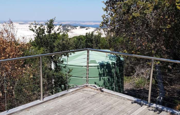 Orion Australia 22000 Ltr Panelled Wall Rainwater Tank accompanying a Tasmanian beach view from a timber deck.