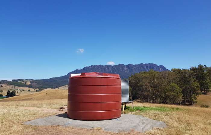 An Orion 22000 Ltr Panelled Wall Rainwater Tank next to steel water tank on open property