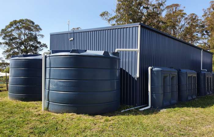 Two 22000 Ltr Panelled Wall Rainwater Tanks next to flat roof shed complemented by three smaller slimline tanks