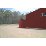 26000 Ltr Panelled Wall Rainwater Tank on gravel next to red shed